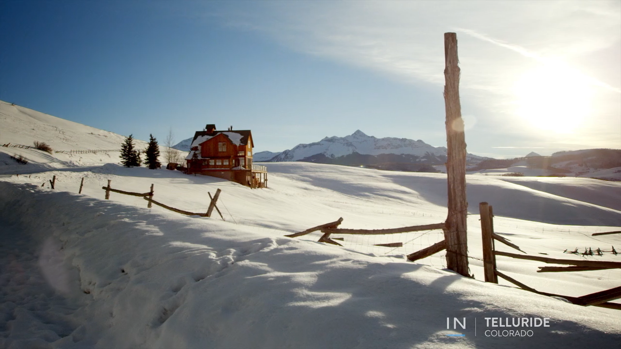 Snowy mountainside with a red cabin shining in the bright sun in Telluride