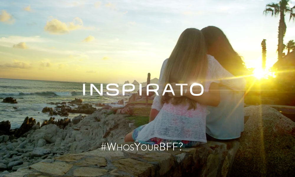 Two women embracing on a rock at the beach during sunset