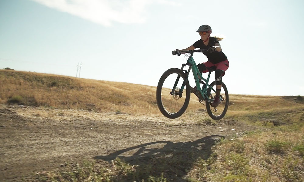 Woman riding an aqua bike wearing a matching aqua helmet and sunglasses riding at sunset.