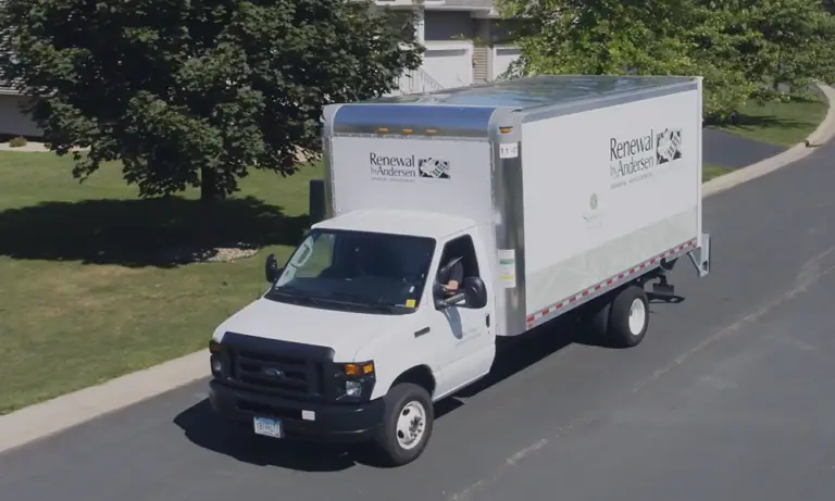 Large truck with renewal by andersen logo on it on a residential street