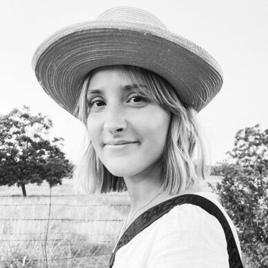 Black and white portrait of a smiling woman in a hat with a blurred natural background.