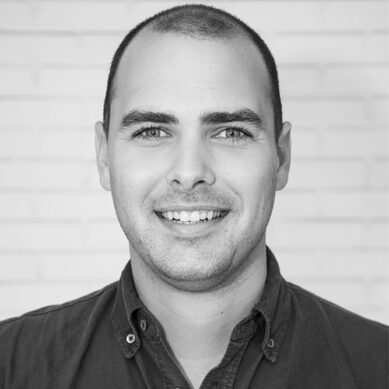 Portrait of a smiling man with a buzzcut, wearing a dark collared shirt.